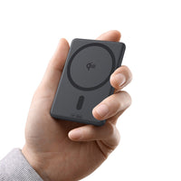 Hand holding a black Qi2 wireless charging pad against a white background
